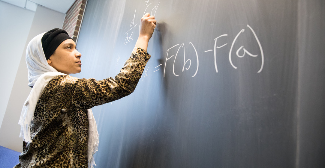 Female student drawing math equations on black board with chalk